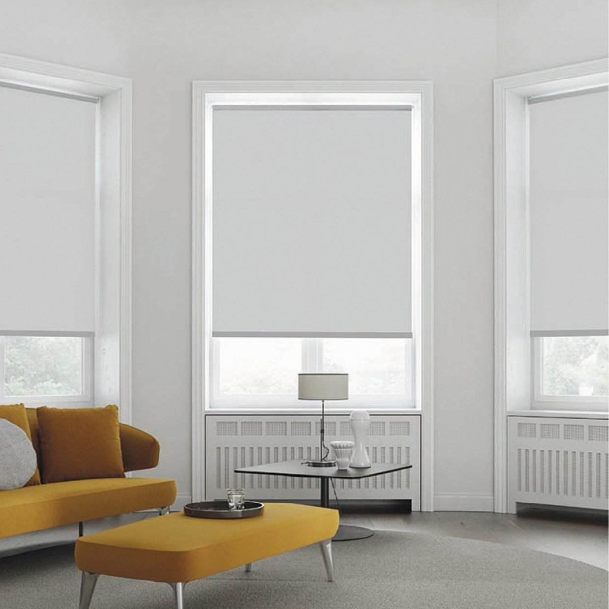 A bright living room with plain roller shades at three windows